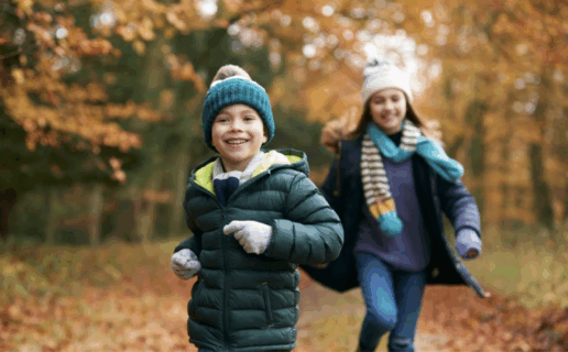 Two kids running in the woods in the fall